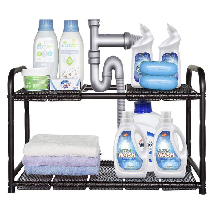 A shelf displays laundry supplies, including detergent, fabric softener, and towels, arranged neatly above a visible pipe connection, suggesting a utility area.