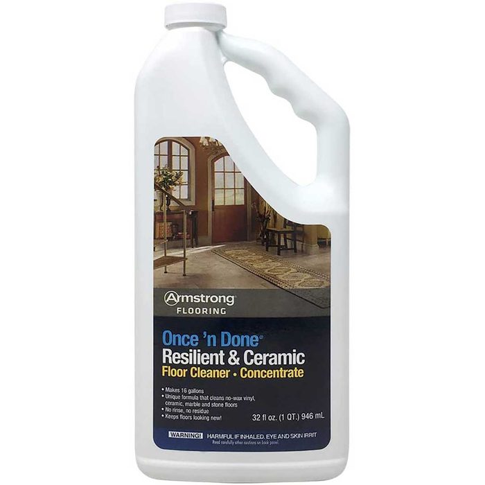 A white plastic jug labeled “Armstrong Flooring Once 'n Done Floor Cleaner” stands upright, featuring an image of a well-furnished interior with a table and decorative items.