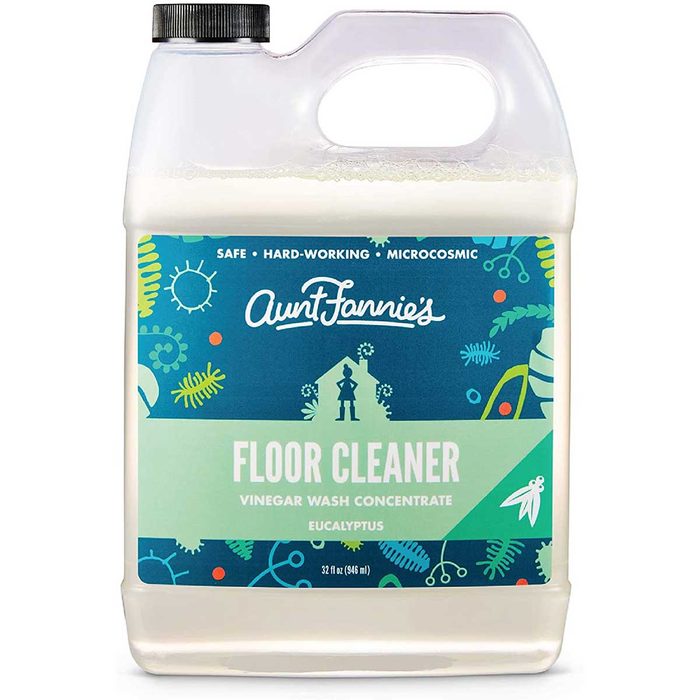 A transparent container of floor cleaner sits upright, labeled with colorful graphics, indicating it is a vinegar wash concentrate in eucalyptus scent.