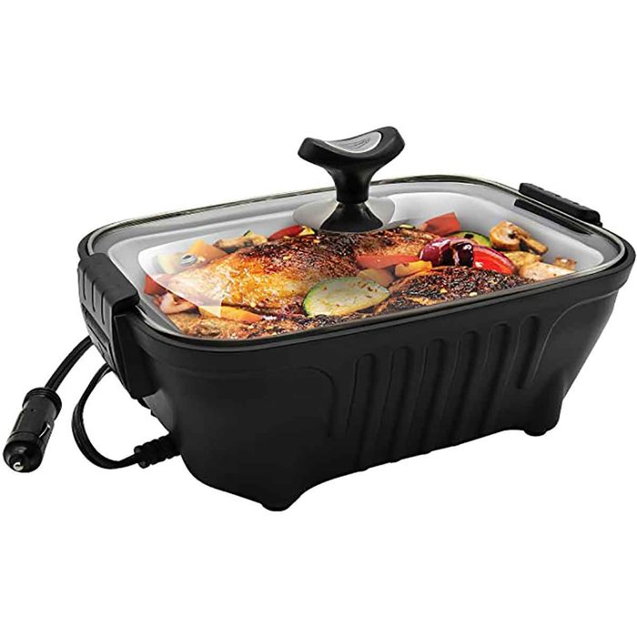 An electric cooking pot holds grilled chicken and vegetables, with a glass lid for visibility. It has a power cord attached for heating purposes.