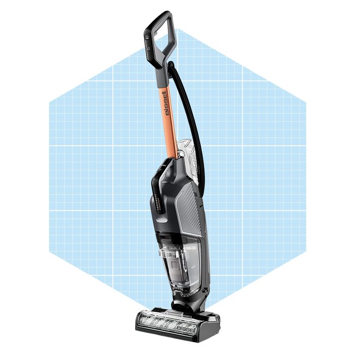 A vacuum cleaner stands upright, designed for cleaning surfaces, showcased against a light blue geometric background, emphasizing its modern features and functionality.