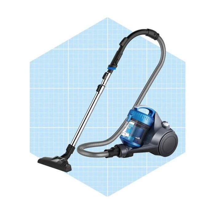 A canister vacuum cleaner stands upright, with a flexible hose and nozzle attached. Its blue and gray design is set against a light blue grid background.