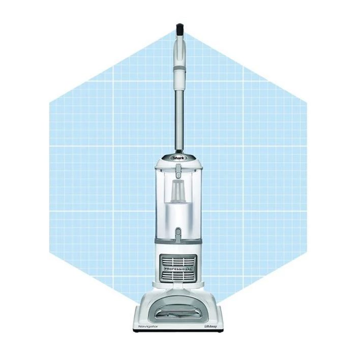 A vacuum cleaner stands upright, designed for cleaning surfaces, positioned against a light blue grid background. It features a clear dust container and silver accents.