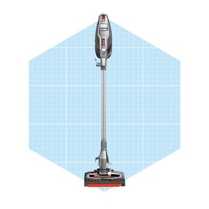 A stick vacuum cleaner stands upright, ready for use, set against a light blue grid background, indicating a modern, clean environment.