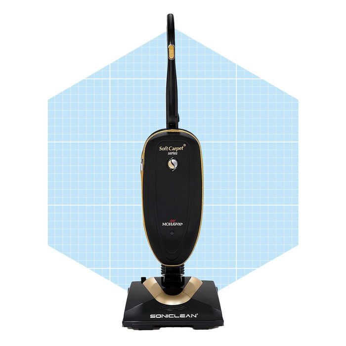 A black and gold carpet vacuum cleaner stands upright against a light blue, grid-patterned background, ready for use on soft carpets.