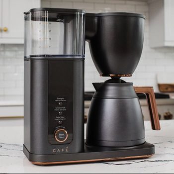 A sleek black coffee maker brews coffee into a matching pot, set on a light marble countertop in a modern kitchen environment.