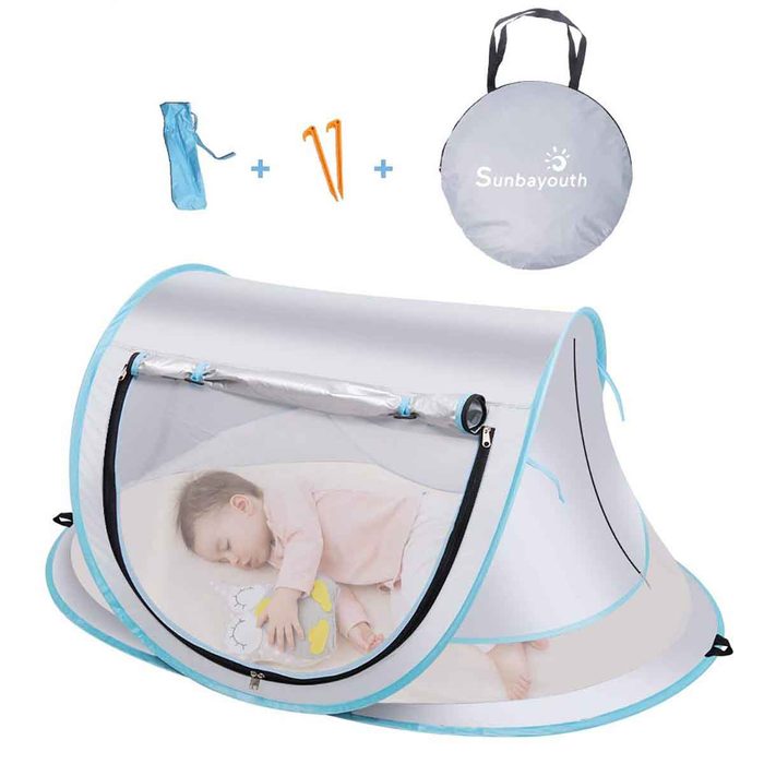 A baby sleeps inside a lightweight tent, featuring a mesh window. The tent is secured with stakes and includes a carrying bag.