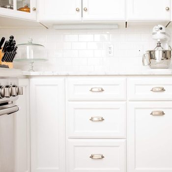 A kitchen corner features white cabinetry, a metal mixing bowl, and a stand mixer, with a knife set and glass display stand near a marble countertop.