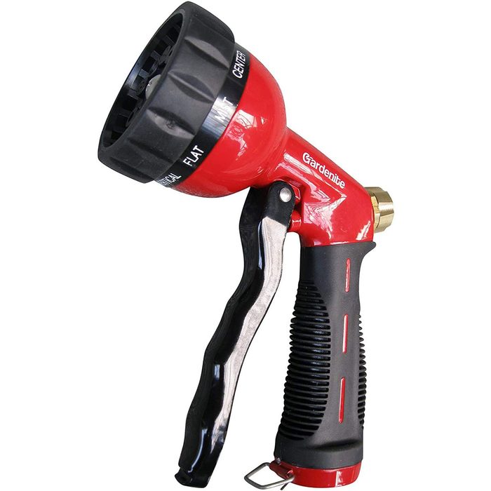 A red garden hose nozzle is held in a hand, designed for watering plants with various spray patterns. The environment is likely a garden or outdoor area.