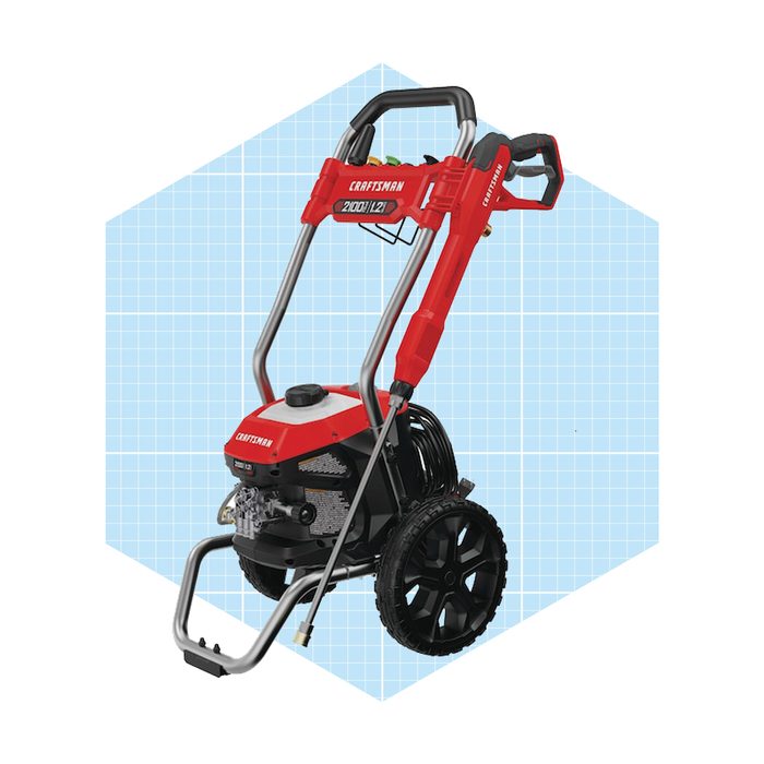 A red and black pressure washer stands upright, equipped with two wheels and a handle, on a light blue grid background, ready for outdoor cleaning tasks.
