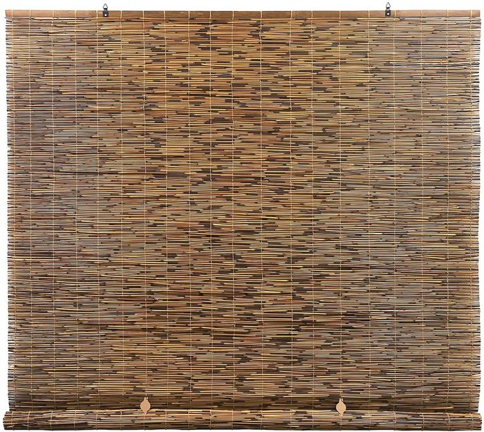 A bamboo window shade hangs vertically, filtering light in a room, offering a natural, textured appearance with alternating brown tones.