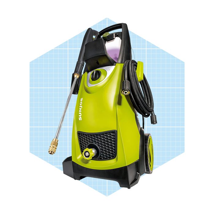 A green pressure washer stands upright, connected with a spray wand and cables, set against a light blue geometric background.