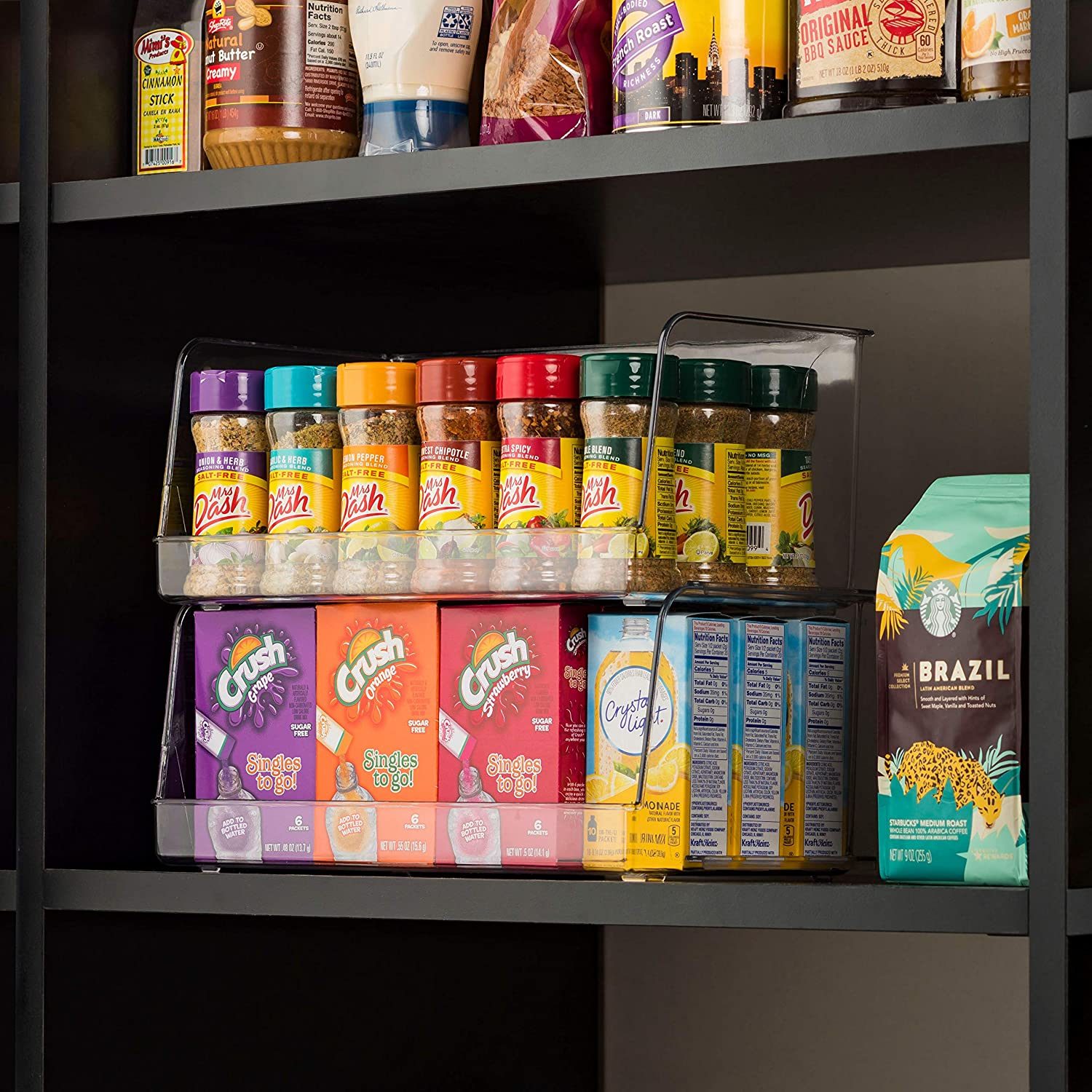 Containers of spices and drink mixes are neatly organized on a black shelf, with various flavors displayed in a clear, tiered storage rack.