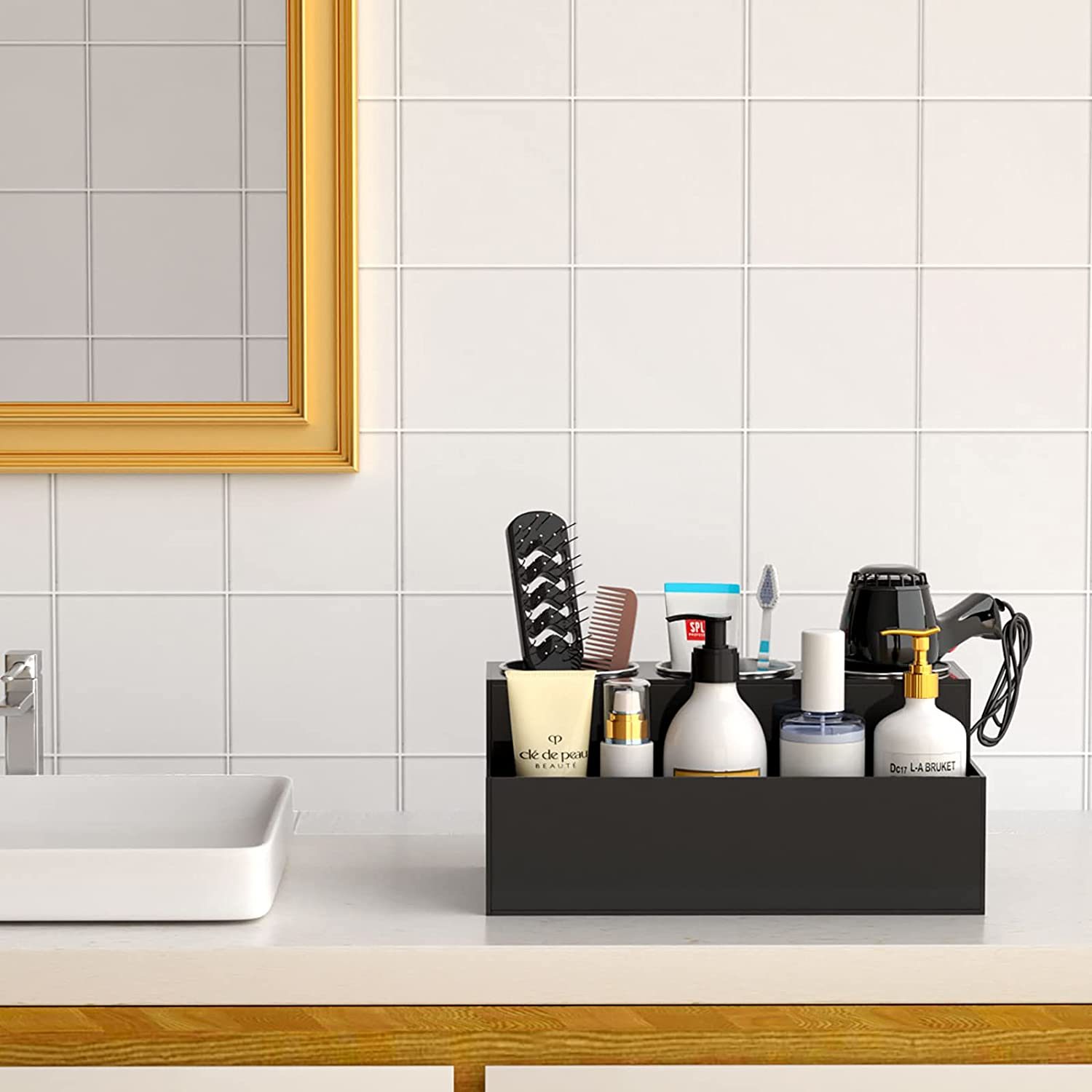 A black organizer holds various skincare and haircare products on a clean bathroom counter, with a mirror and tiled wall in the background.