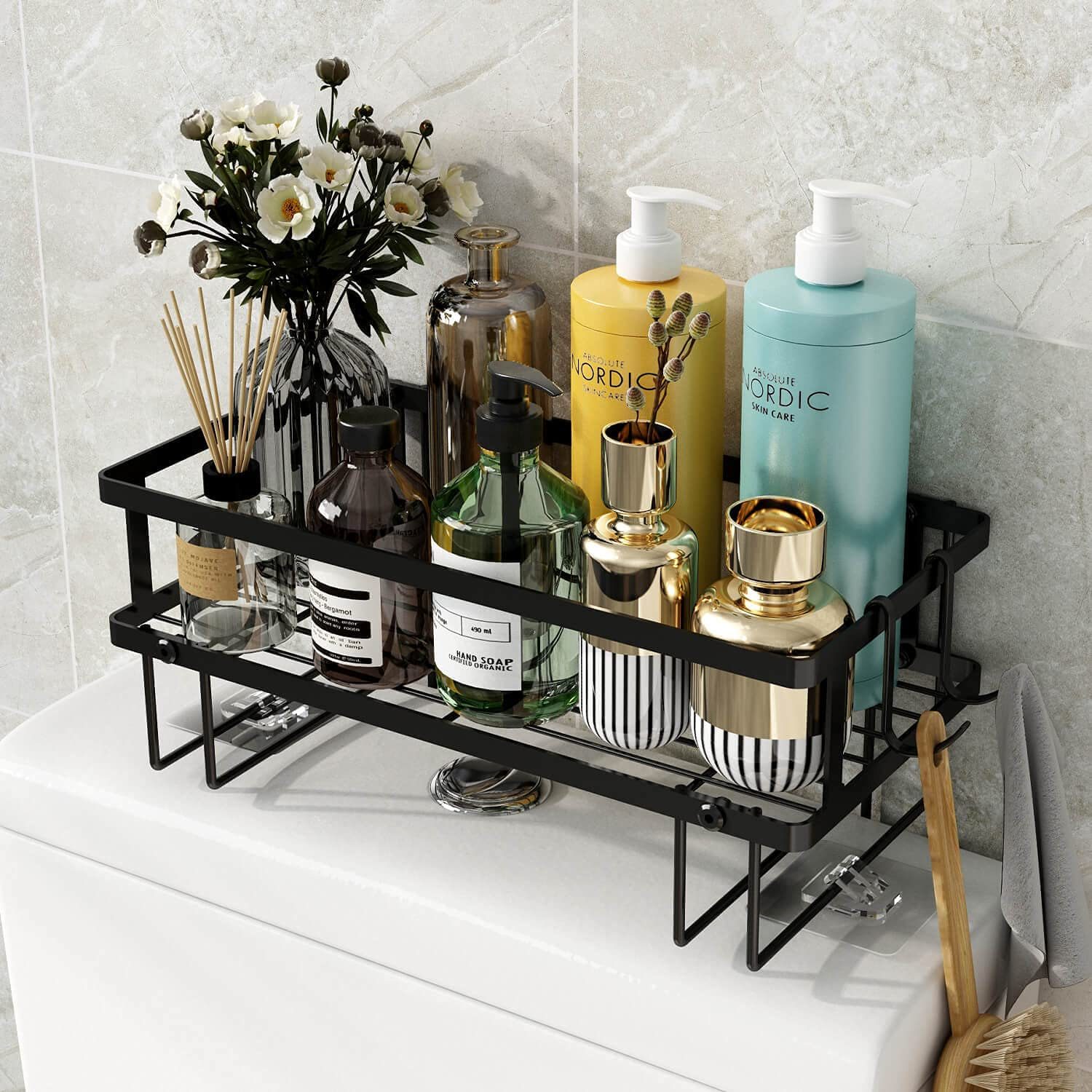 A black metal tray holds various bottles of skincare products and decorative items atop a white surface, set against grey tiled walls in a bathroom.