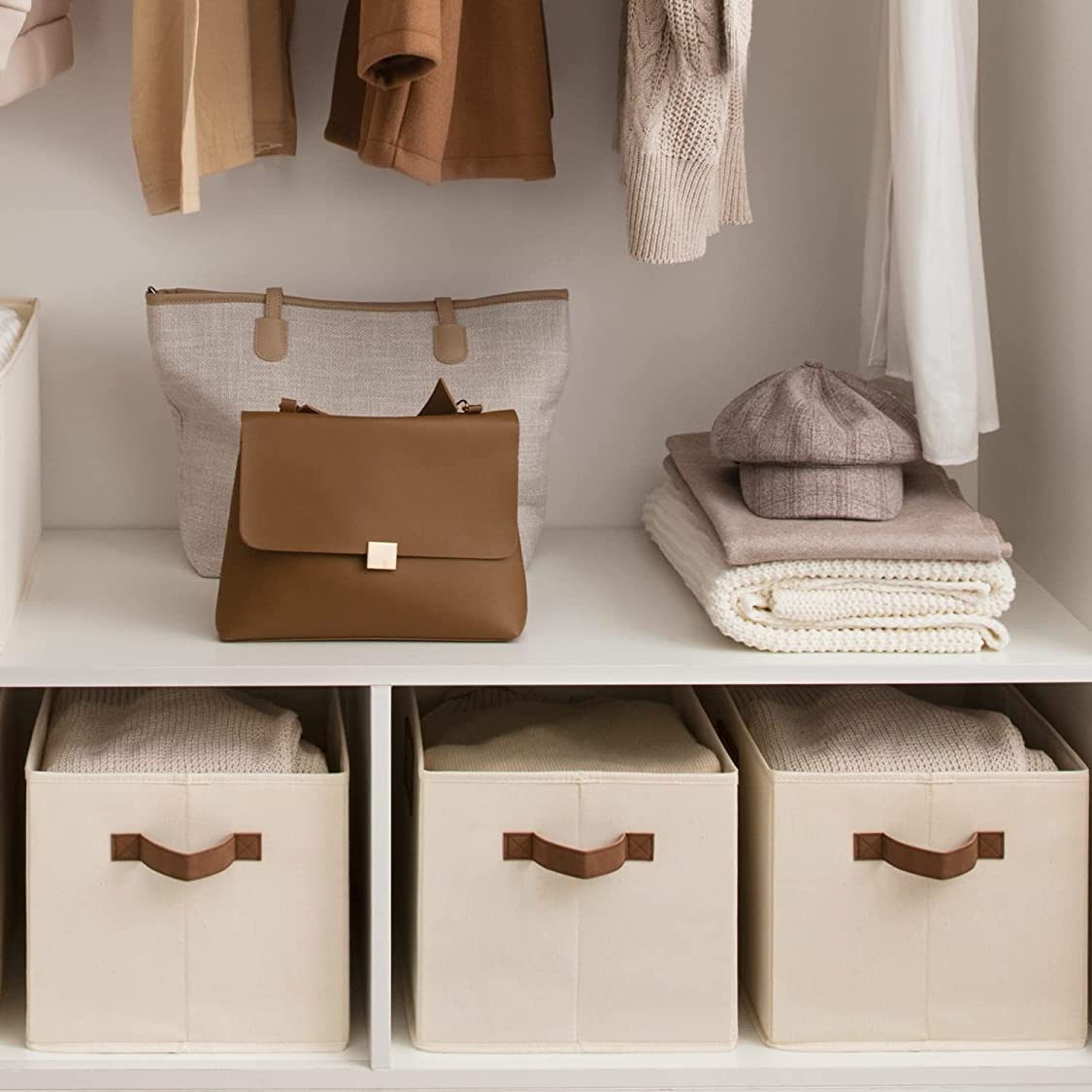 A brown handbag and a tote sit on a shelf, surrounded by clothing and folded blankets in neatly organized storage bins below.