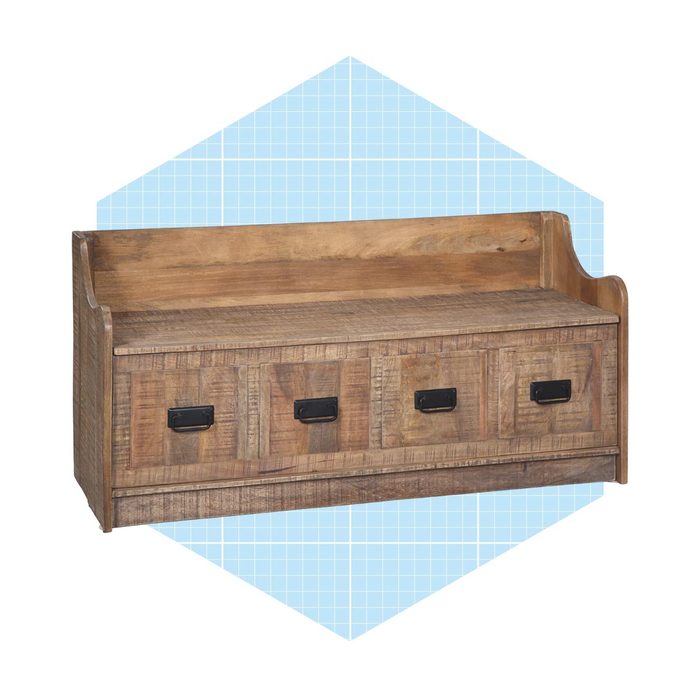 A wooden bench with a backrest stores items in three front drawers, placed against a pale blue geometric background.