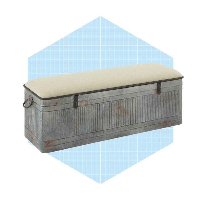 A metal storage bench features a cushioned lid, positioned against a light blue geometric background, providing a stylish and functional furniture piece.