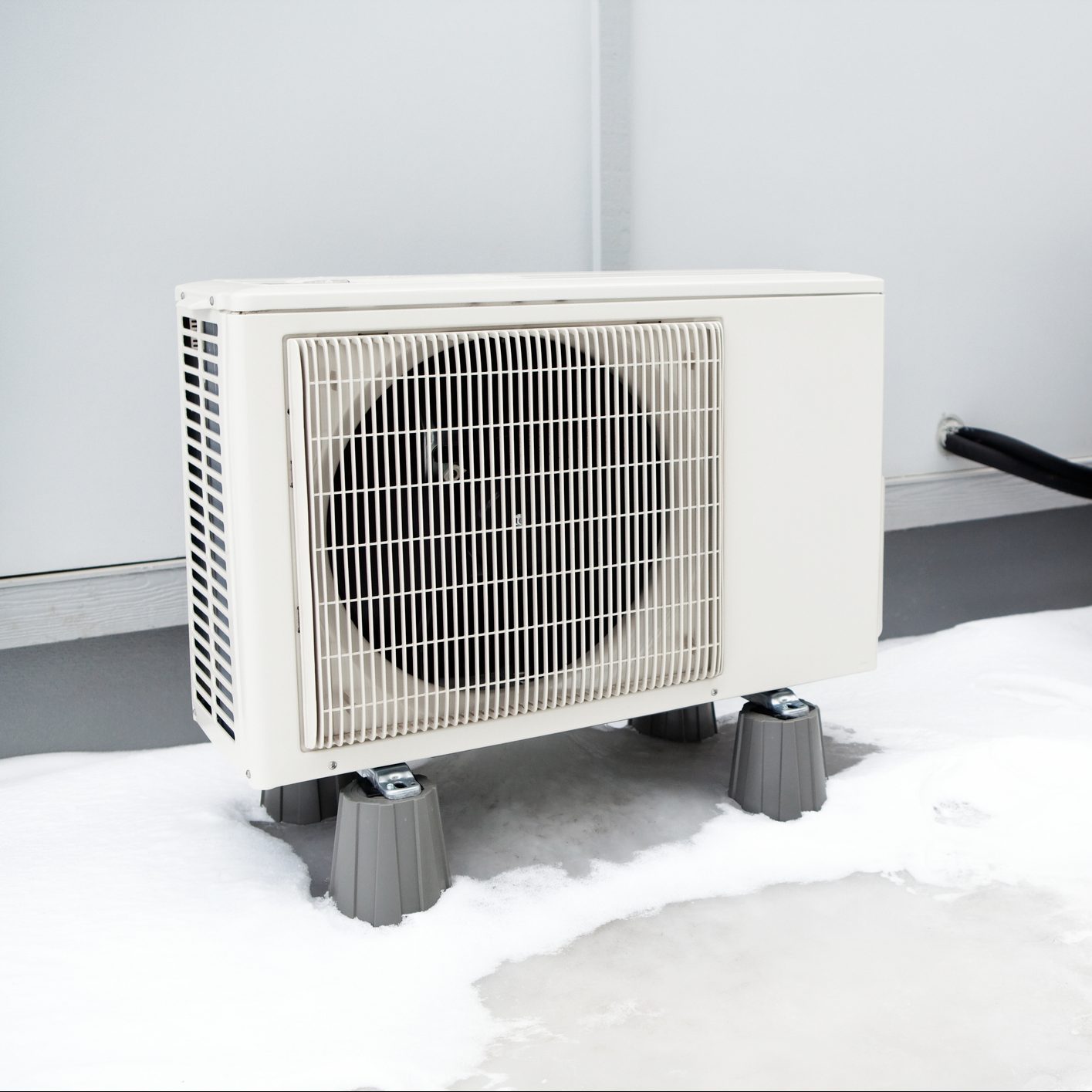 An air conditioning unit stands on plastic supports, surrounded by a puddle of foam on a gray floor in a minimalistic indoor setting.