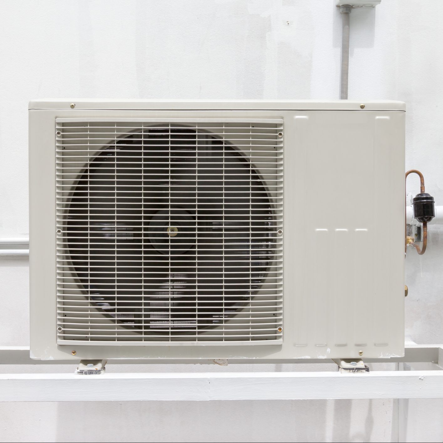 A gray air conditioning unit rests against a white wall, with a large fan visible at the front, providing ventilation in a residential or commercial setting.