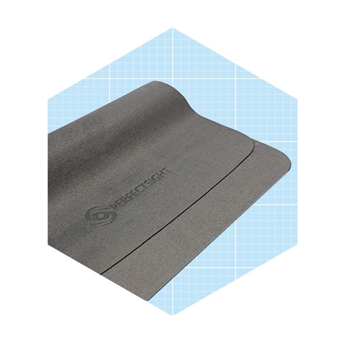 A gray yoga mat lies flat, featuring a logo, on a light blue grid background, ready for use in a fitness or relaxation context.