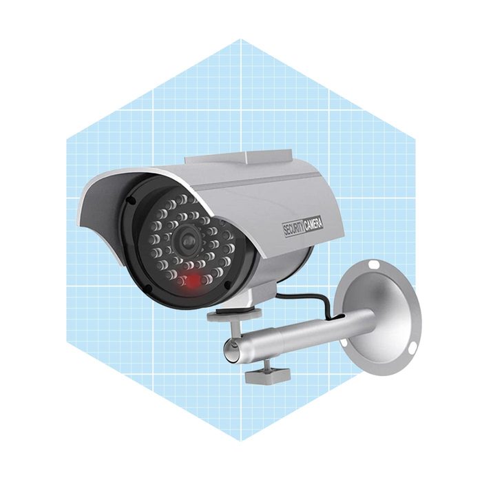 A security camera is mounted on a wall, actively monitoring the area, set against a light blue grid background.