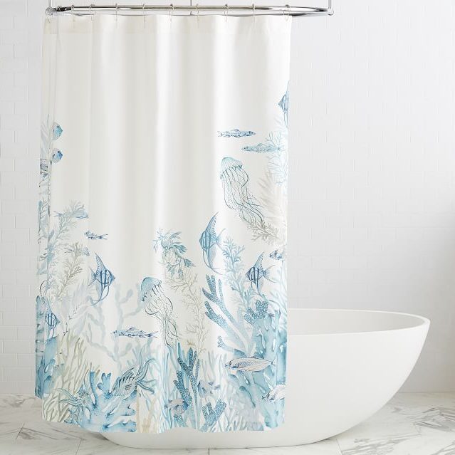 A shower curtain adorned with aquatic illustrations hangs above a white, freestanding bathtub in a bright, tiled bathroom.