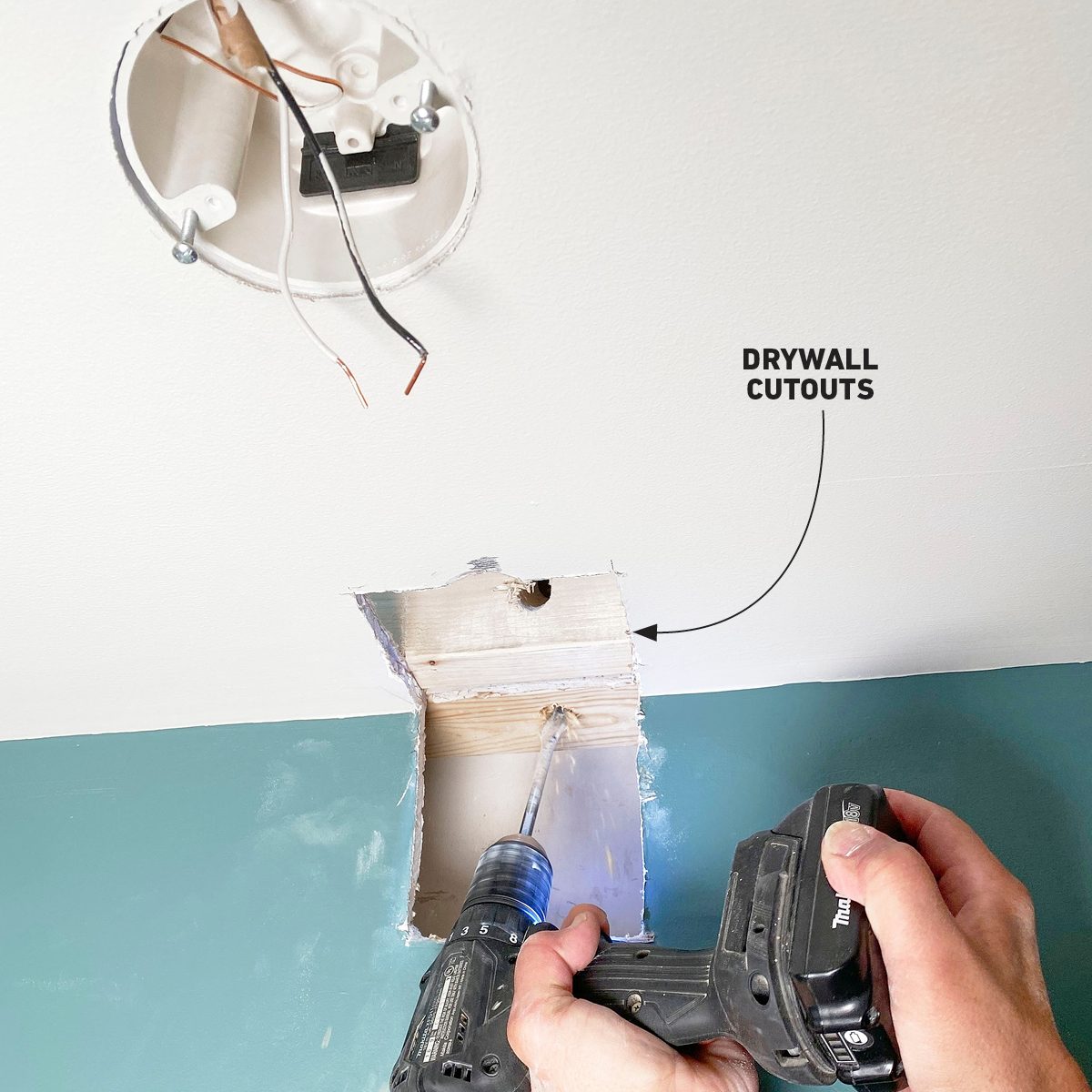 A person uses a power drill to create drywall cutouts on a wall, revealing electrical components above, in a home improvement context.