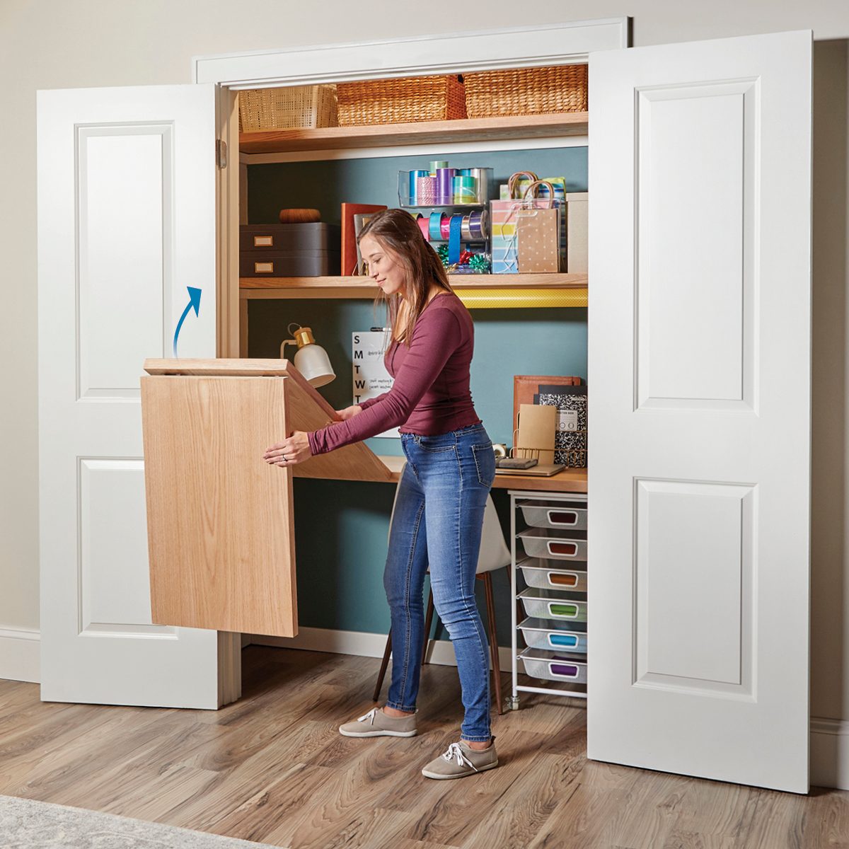 A woman pulls out a wooden foldable desk from a closet, surrounded by organized shelves of decorative boxes and craft supplies in a modern room.
