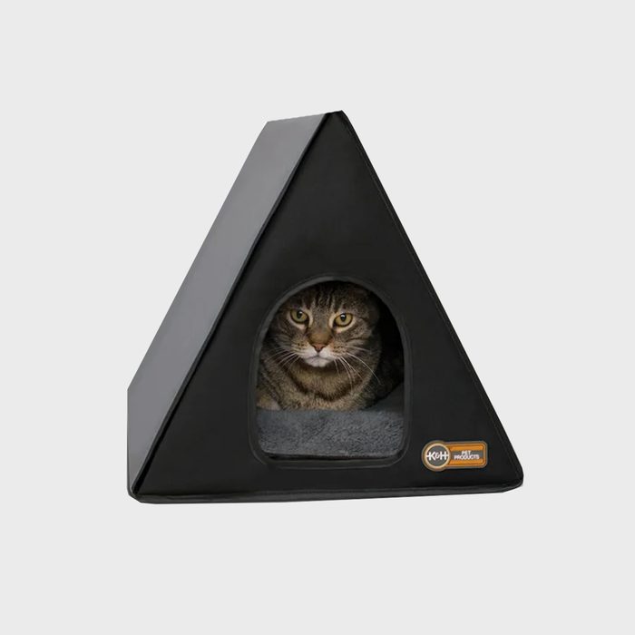 A triangular, black pet house houses a sleeping tabby cat, looking content from its window. The background is neutral and unobtrusive.