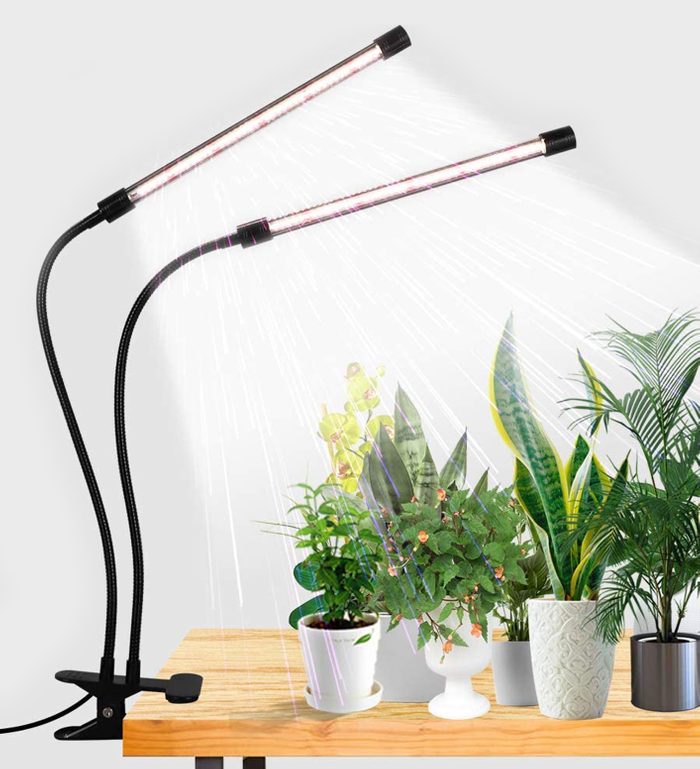 Two flexible light tubes illuminate various potted plants on a wooden table, enhancing their growth in a well-lit indoor environment.