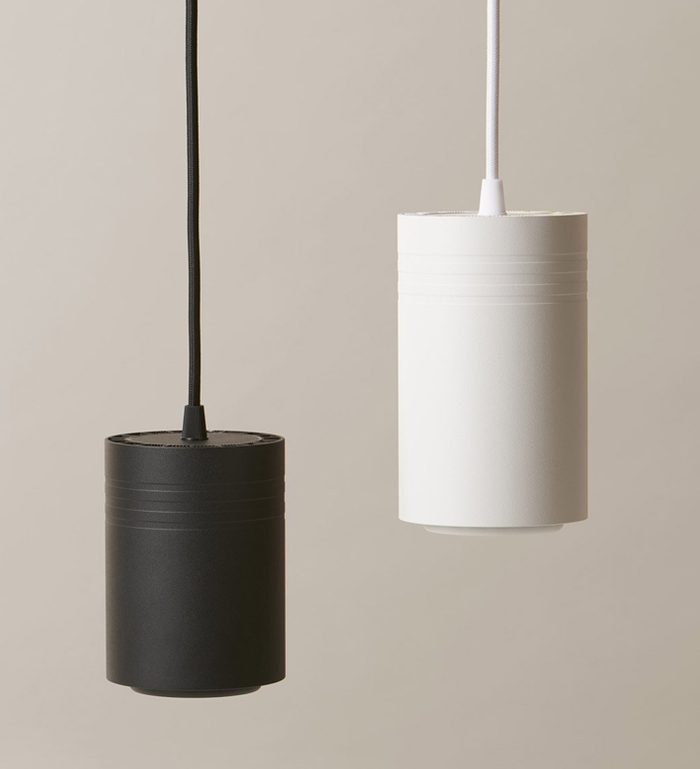 Two cylindrical pendant lights, one black and one white, hang from the ceiling against a neutral background, showcasing a modern minimalist design.