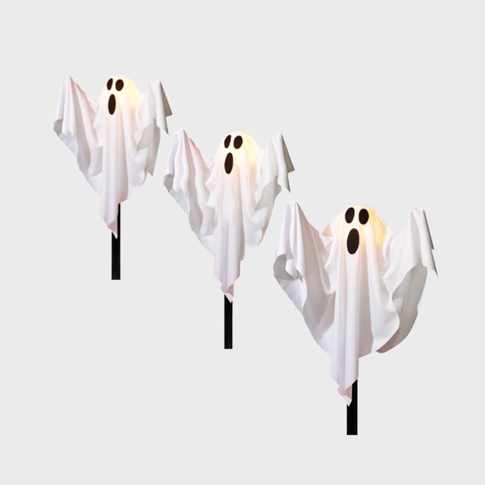 Three white ghost decorations with black eyes and mouths stand on poles, illuminated from within, against a light gray background.