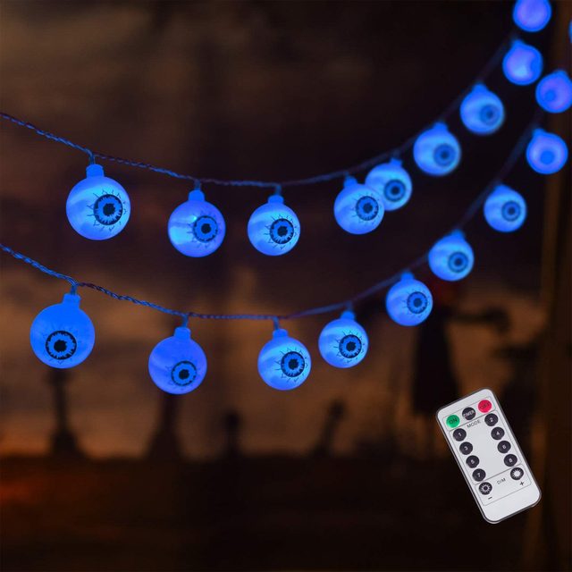 Blue string lights shaped like eyeballs hang against a dark background, creating an eerie atmosphere. A remote control is positioned nearby.