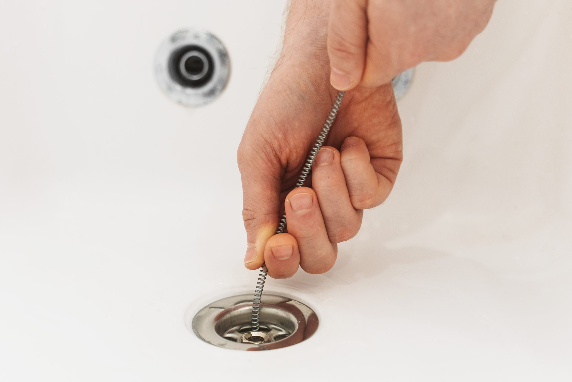 Plumber using drain snake to unclog bathtub.