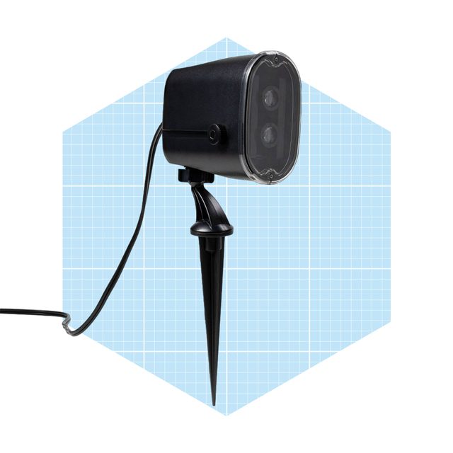 A black landscape spotlight is mounted on a sharp stake, directed forward, with a power cable extending from it against a light blue grid backdrop.