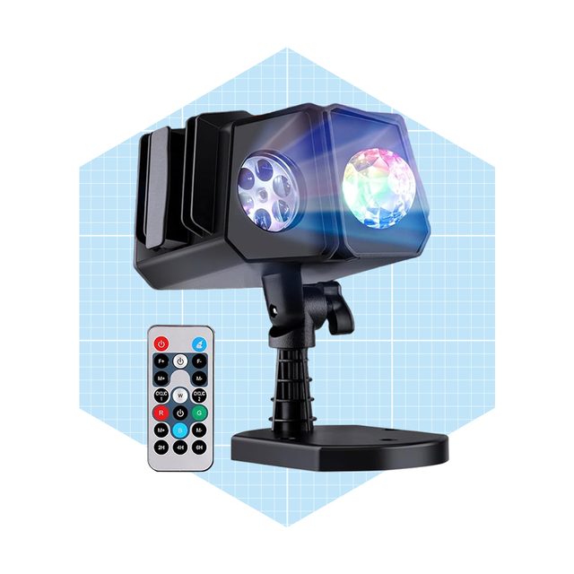 A dual-lens stage light projects colorful beams, mounted on a stand. A remote control is positioned nearby for adjusting settings. The background is light blue grid.