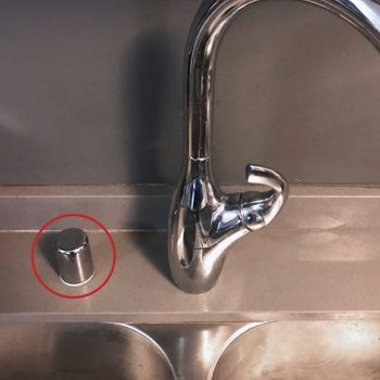 A metal soap dispenser stands beside a shiny kitchen faucet on a smooth countertop, suggesting a clean, functional kitchen environment.