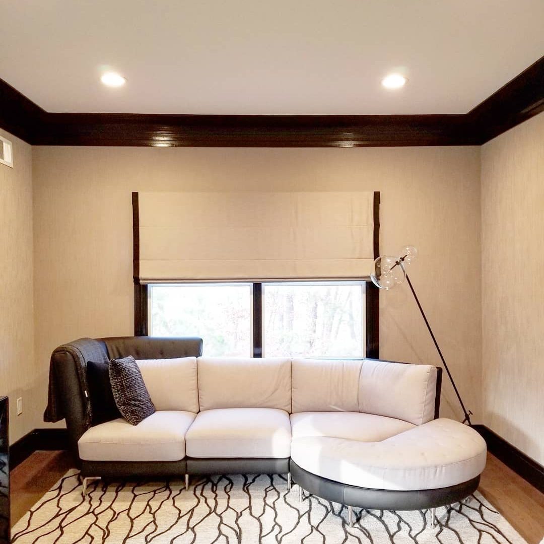 A modern sectional sofa rests in a brightly lit room, adjacent to a large window with blinds, surrounded by neutral-colored walls and wooden trim.