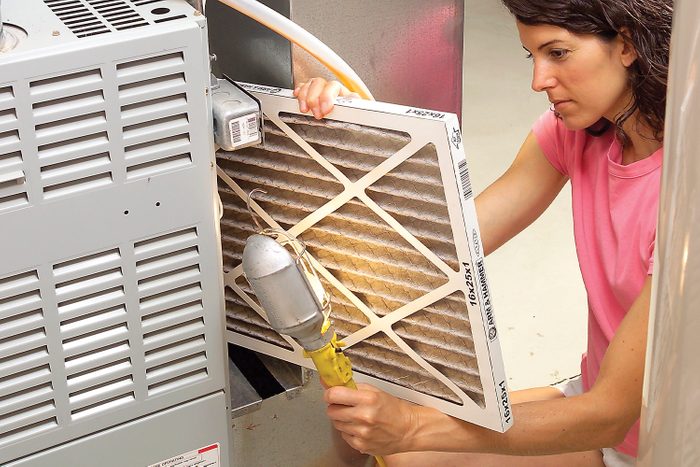 A woman replaces a dirty air filter in a gray appliance, using a tool, in a well-lit, indoor space.
