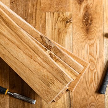Wooden planks rest on a wooden surface, while a hammer and chisel lay nearby, suggesting preparation for construction or woodworking activities.