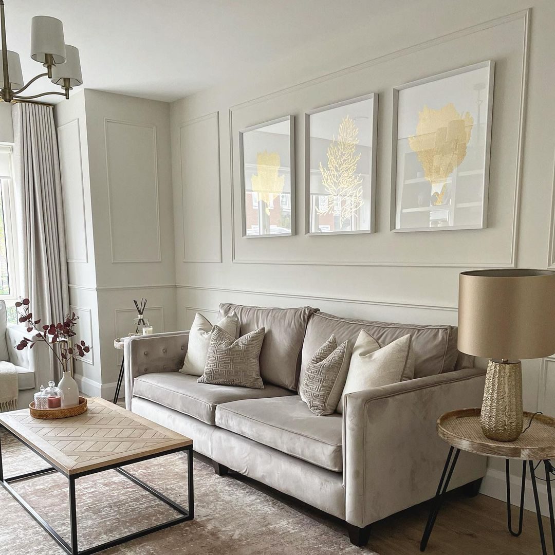 A beige sofa with decorative pillows sits across from a wooden coffee table in a tastefully decorated living room featuring framed art and a lamp.