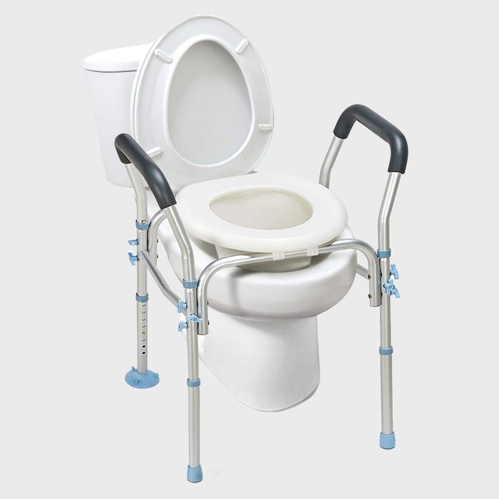 A toilet with a padded raised seat and metal safety frame provides support. The environment is neutral, enhancing accessibility for users with mobility challenges.
