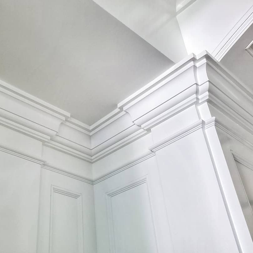 A white ceiling meets elegantly detailed white crown molding, framing a bright, minimalist interior space characterized by clean lines and a light color palette.