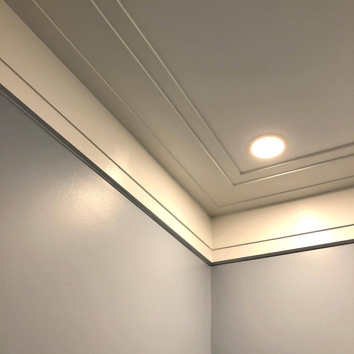 A ceiling corner features crisp white molding, illuminated by a recessed light, above a smooth, light blue wall, creating a clean, modern aesthetic.