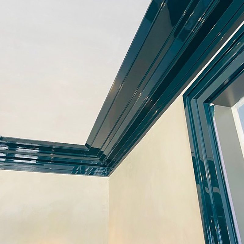 Polished dark trim lines intersect at the corner of a light-colored wall and ceiling, creating a sleek, modern aesthetic in an indoor space.