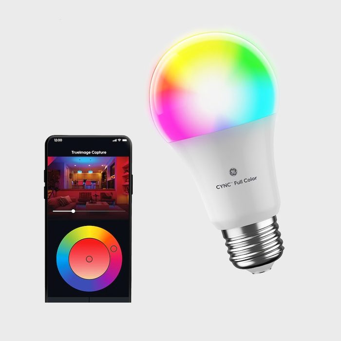 A multicolored smart light bulb is illuminated, while a smartphone displays a color selection interface for adjusting the bulb's colors in a modern setting.