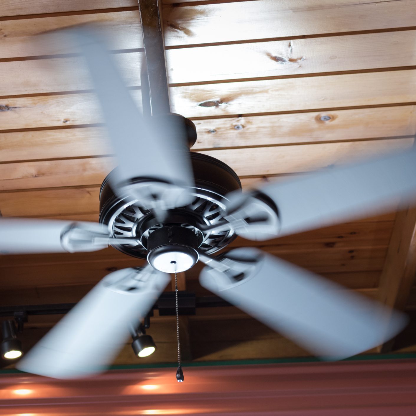 A ceiling fan spins rapidly, dispersing air in a wooden-paneled room, enhancing comfort under soft lighting from adjacent fixtures.