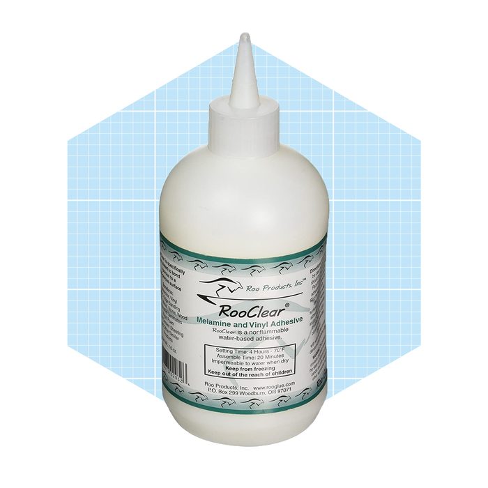 A white bottle of adhesive stands upright, featuring a pointed nozzle. It's set against a light blue, graph paper-like background.