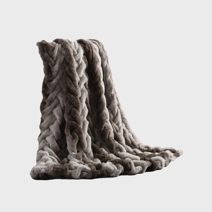 A thick, braided blanket drapes elegantly, showcasing a soft texture and a gradient of gray hues against a plain white background.
